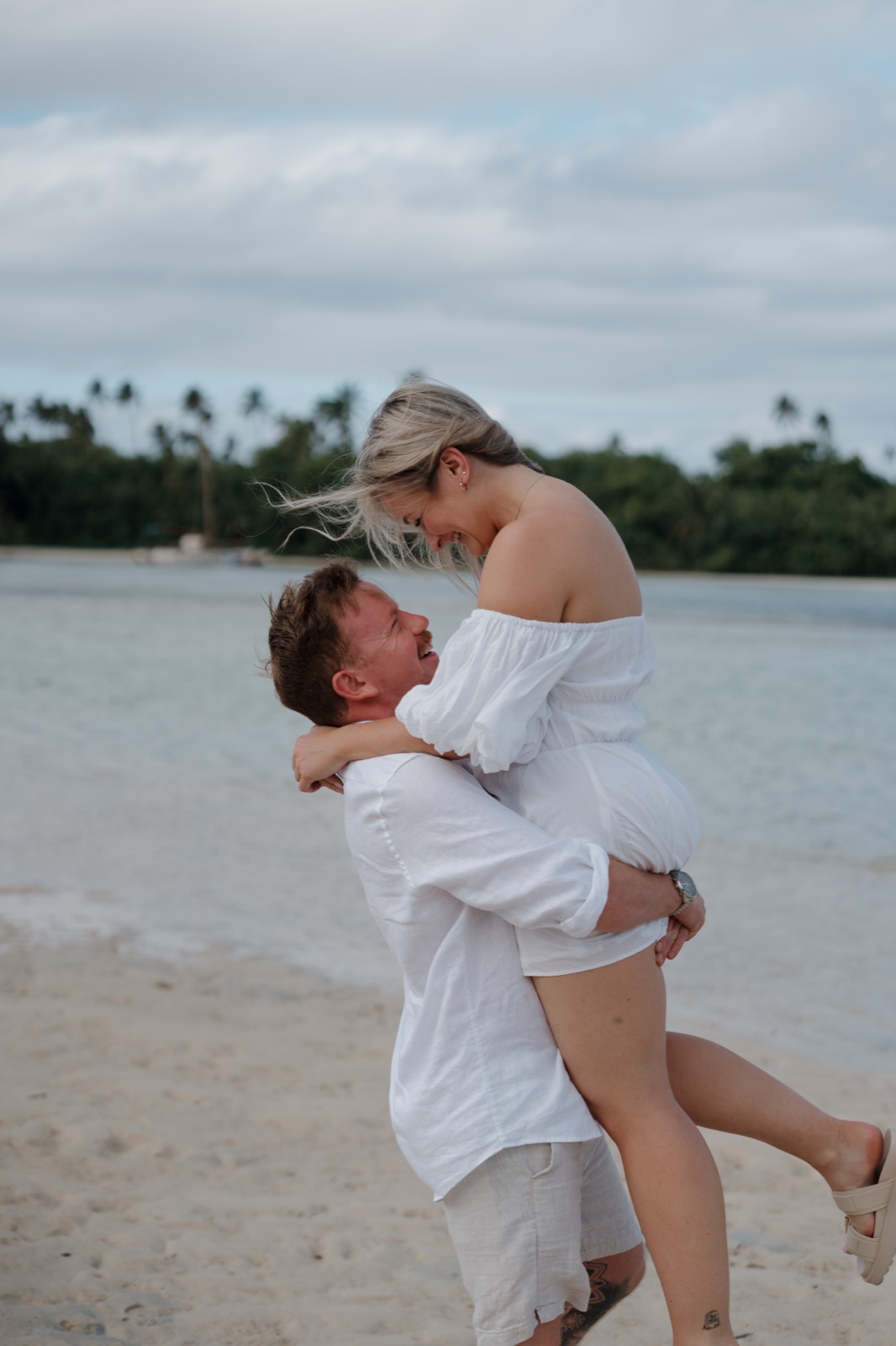 A man lifting his partner into the air on the beach, both laughing