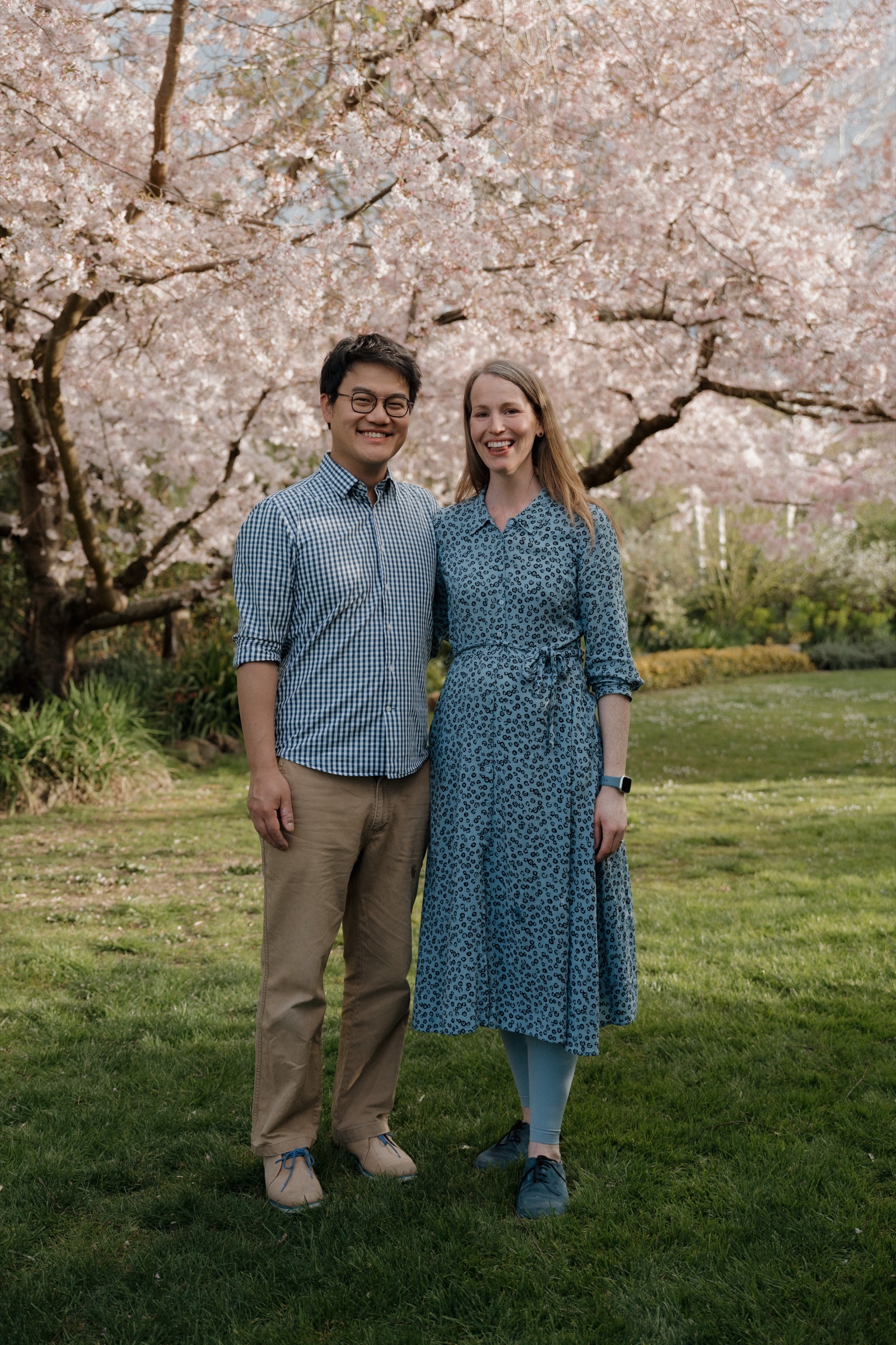 A couple standing close together beneath cherry blossom