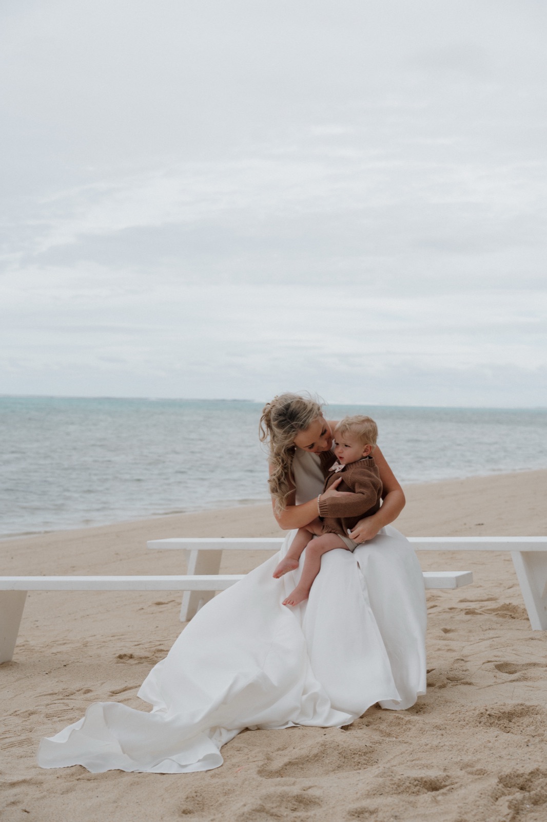 A bride holding a toddler close on a quiet beach