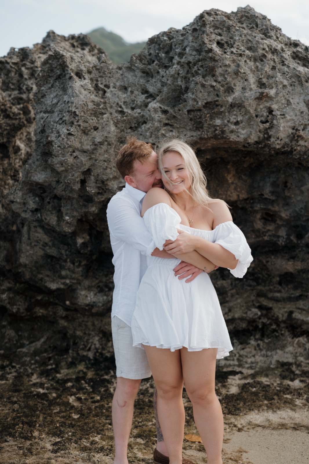 A man wrapping his partner in a hug against a rocky shore