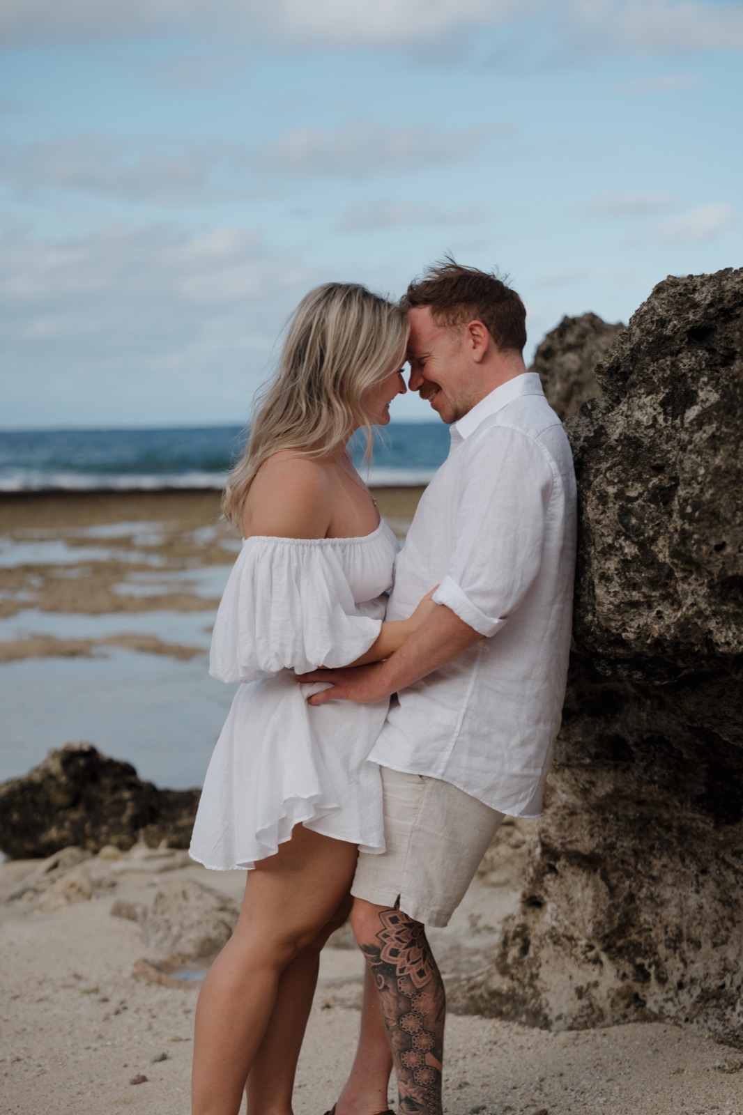 A couple resting their foreheads together on a rocky island beach