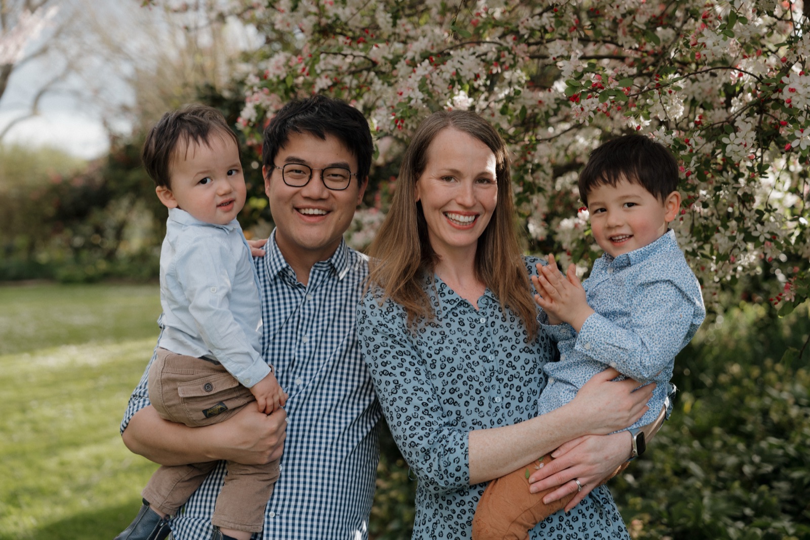 A family of four smiling together beneath a flowering tree