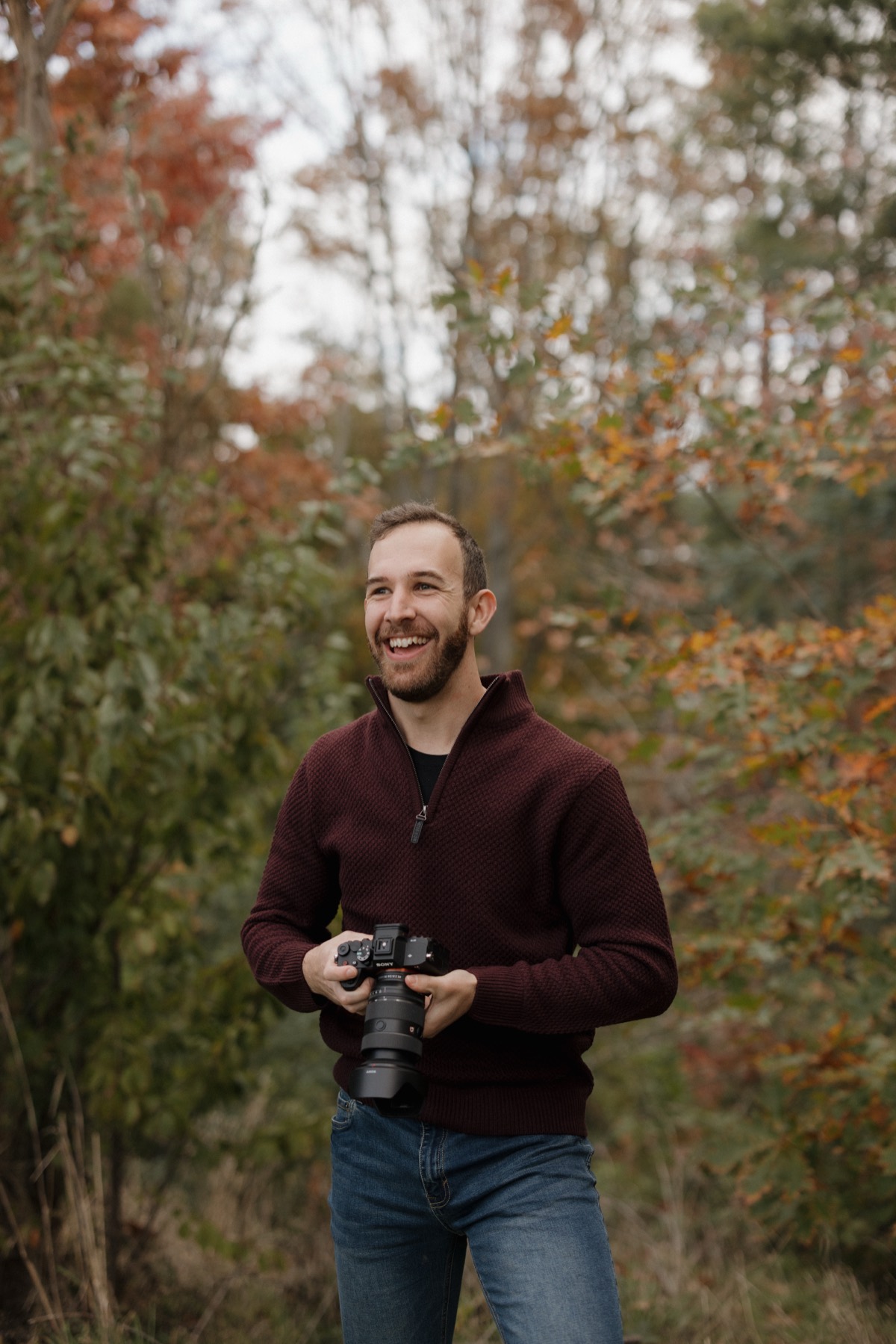 Kowen mid-laugh among autumn trees, camera in hand