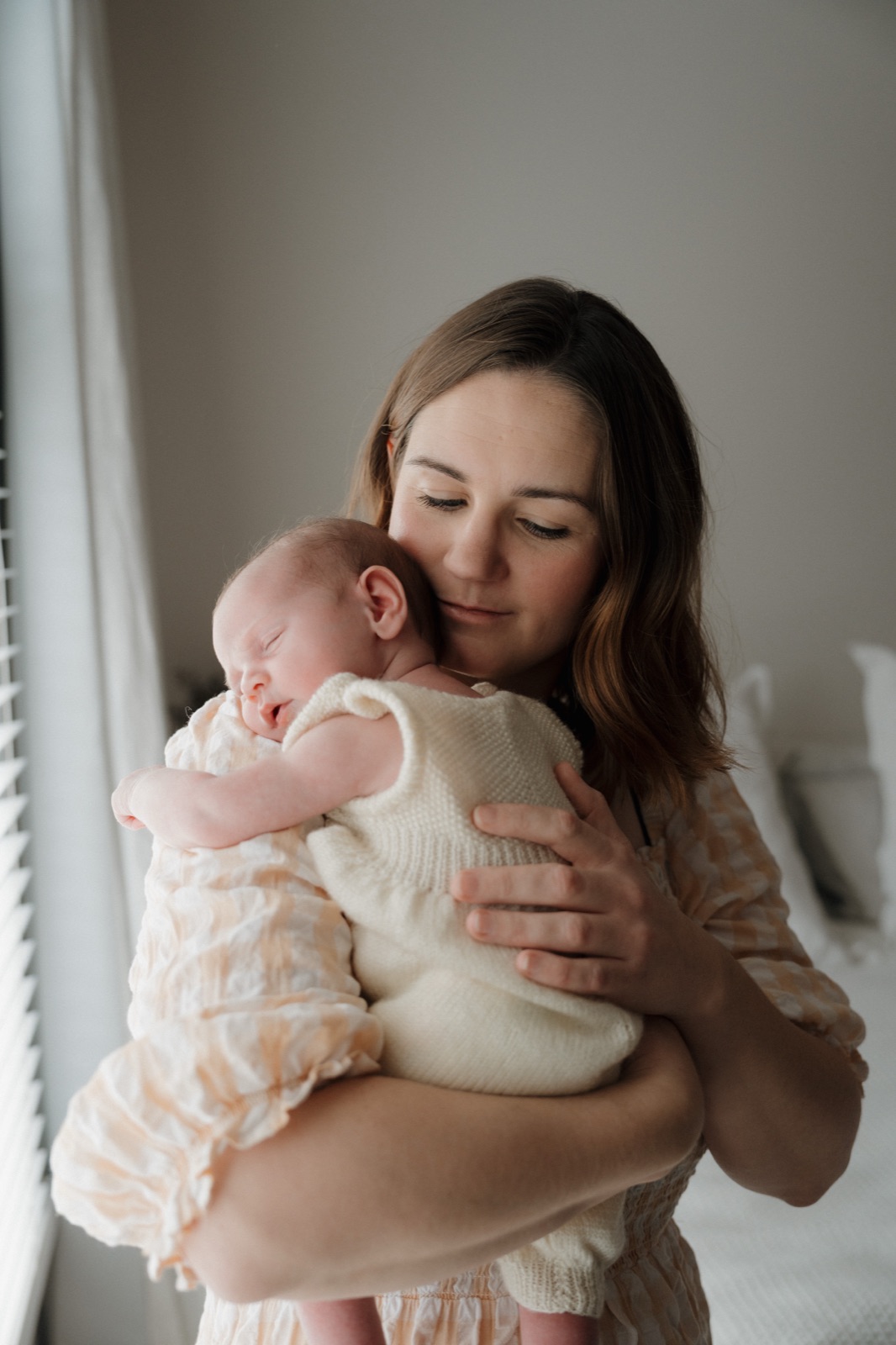 A mother cradling her sleeping newborn by a bright window